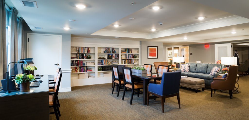 A cozy meeting area with a dining table surrounded by chairs, bookshelves filled with books, and artwork on the wall.