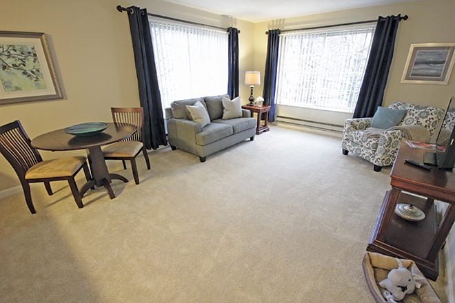 A cozy living room with furniture, including a sofa and armchair, complemented by large windows with curtains.