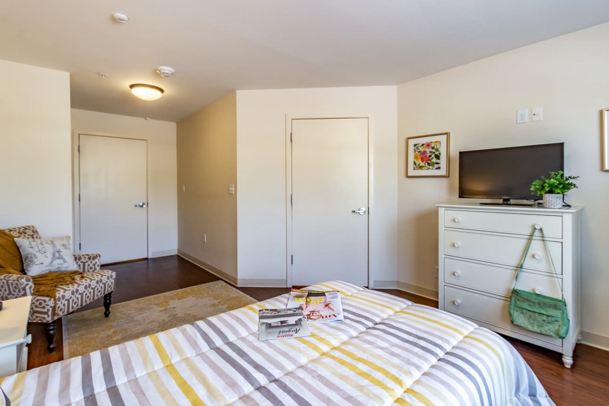 A cozy bedroom featuring a neatly made bed, dresser with a television on top, and simple decor.