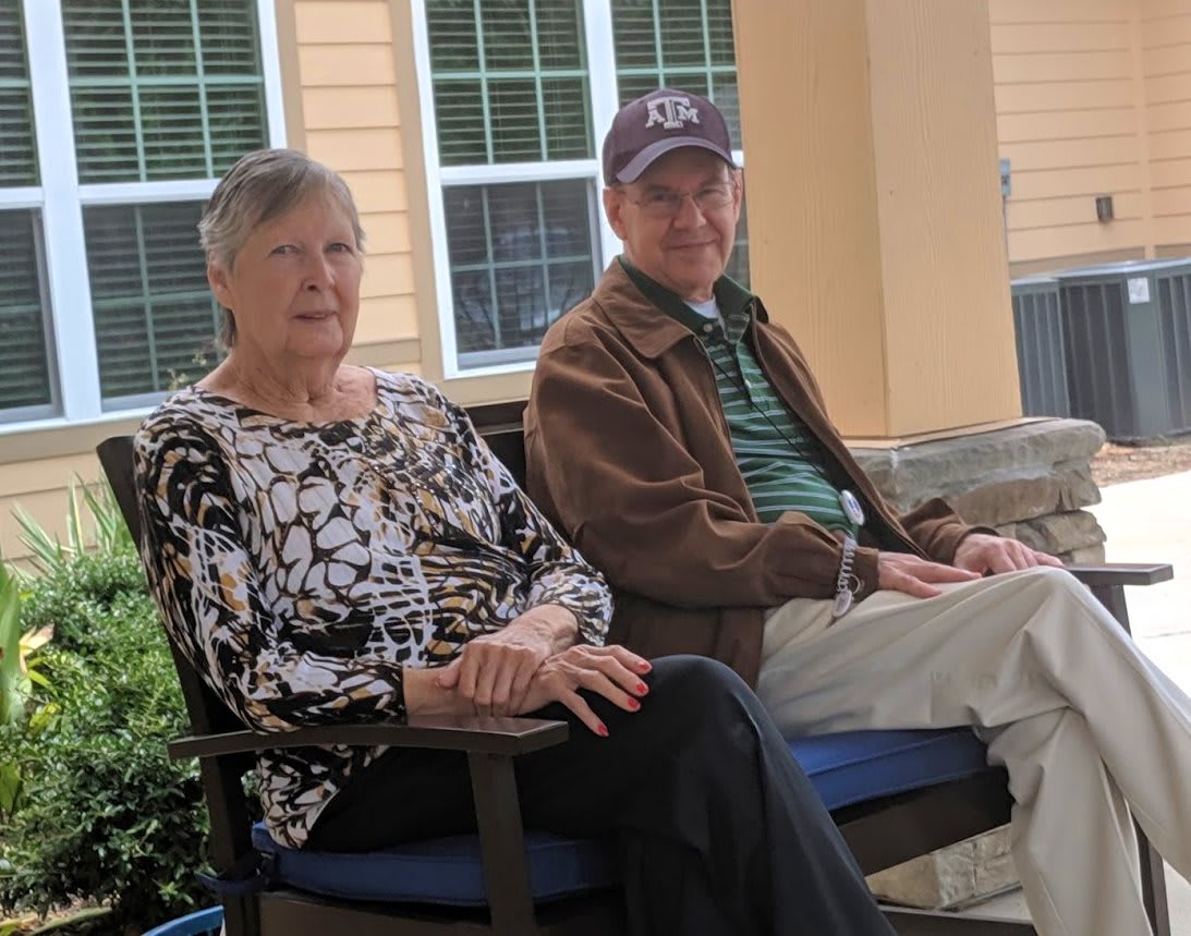 An elderly couple sitting outdoors on chairs, enjoying a relaxed moment.