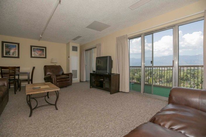 A spacious living room with a TV, sofas, and large windows leading to a balcony.
