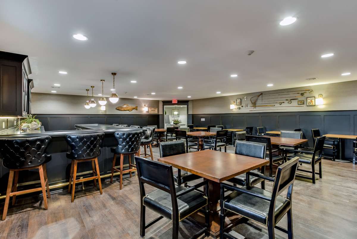 An empty restaurant interior with tables, chairs, and bar stools under warm lighting.