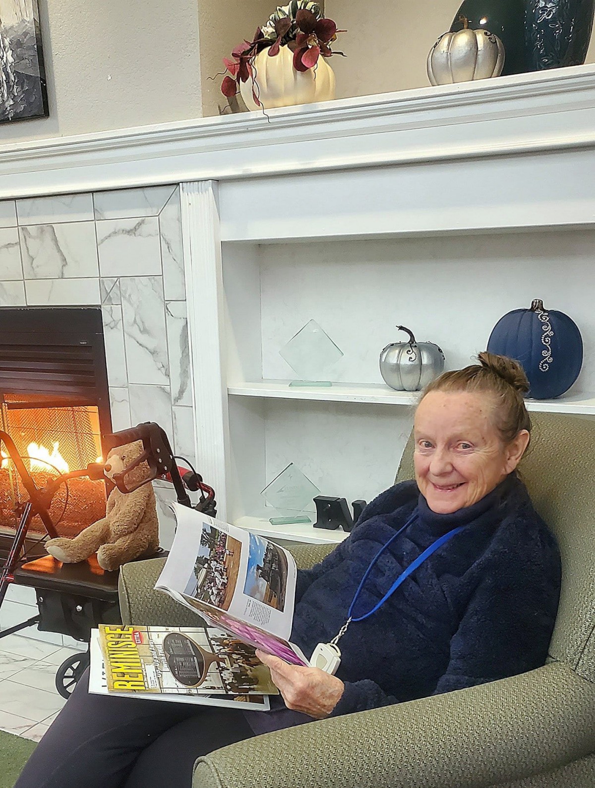 A woman sitting in a cozy chair by the fireplace, reading a magazine.