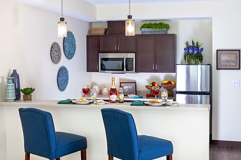 A modern kitchen with a dining area, featuring blue bar stools and elegant pendant lighting.