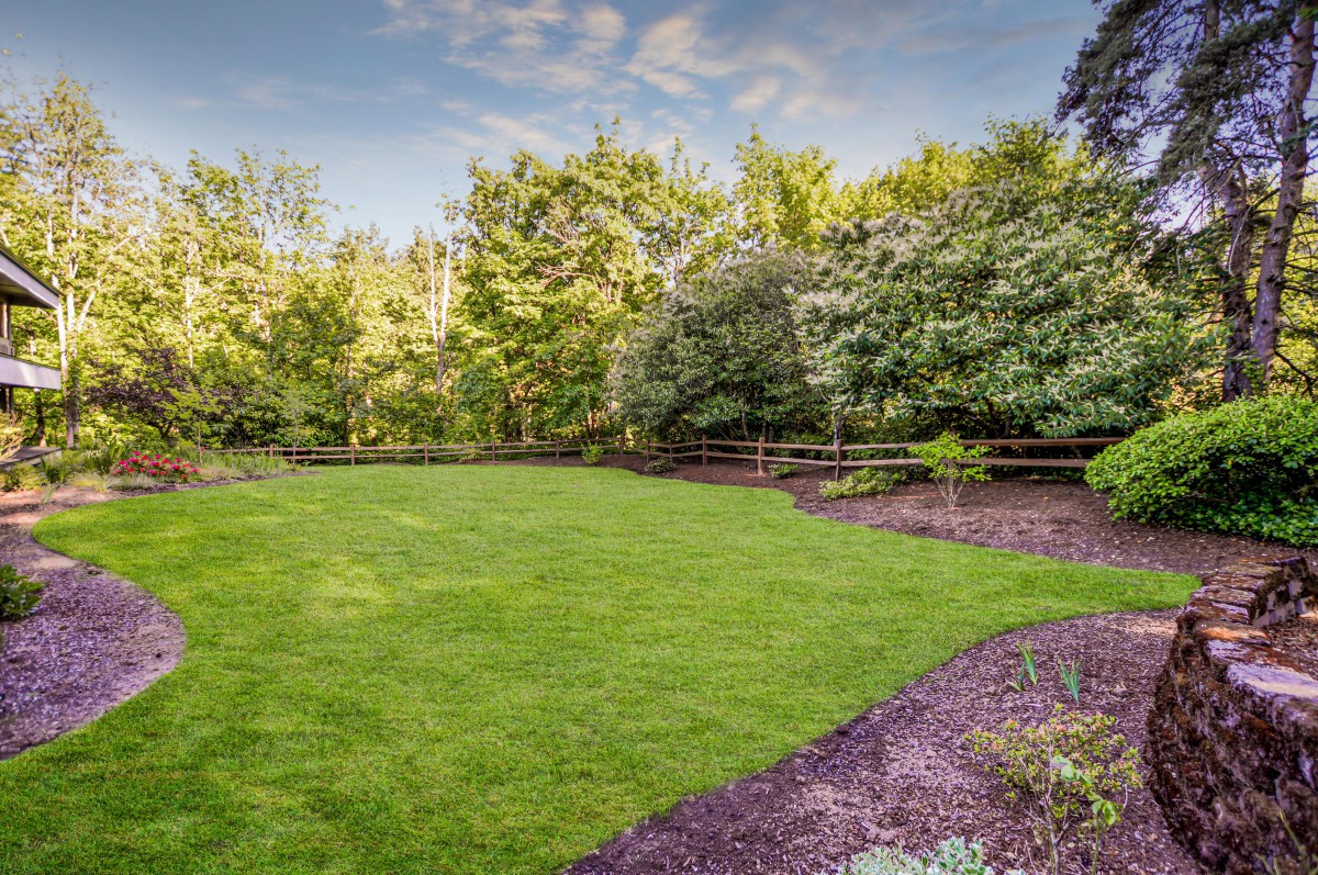 A well-maintained lawn bordered by trees and shrubs, with a wooden fence in the background.