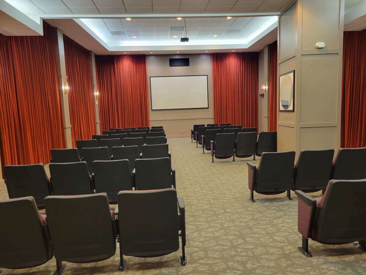 An empty theater room with arranged seats and a projection screen.