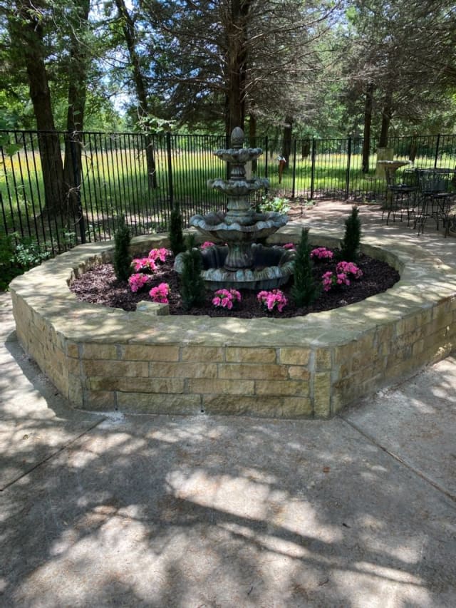 A decorative garden fountain surrounded by flowers and a stone wall.