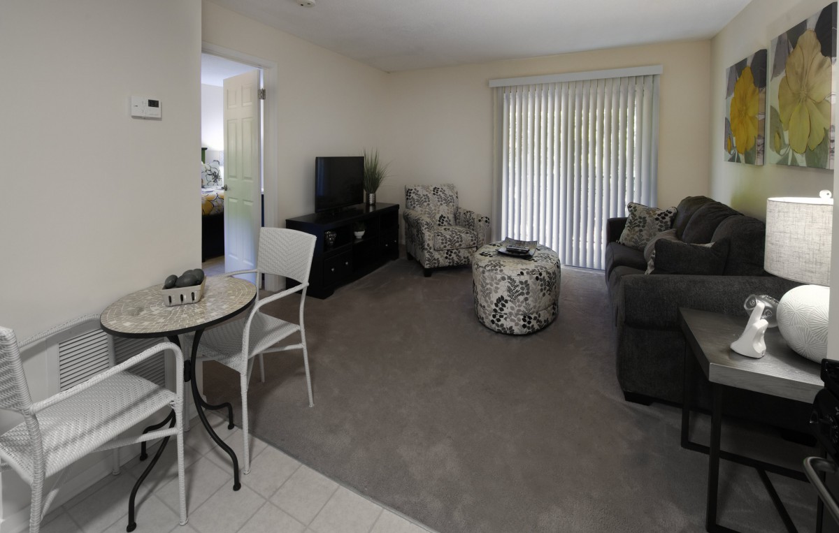 A cozy living room with comfortable seating, a TV, and a sliding door with blinds.