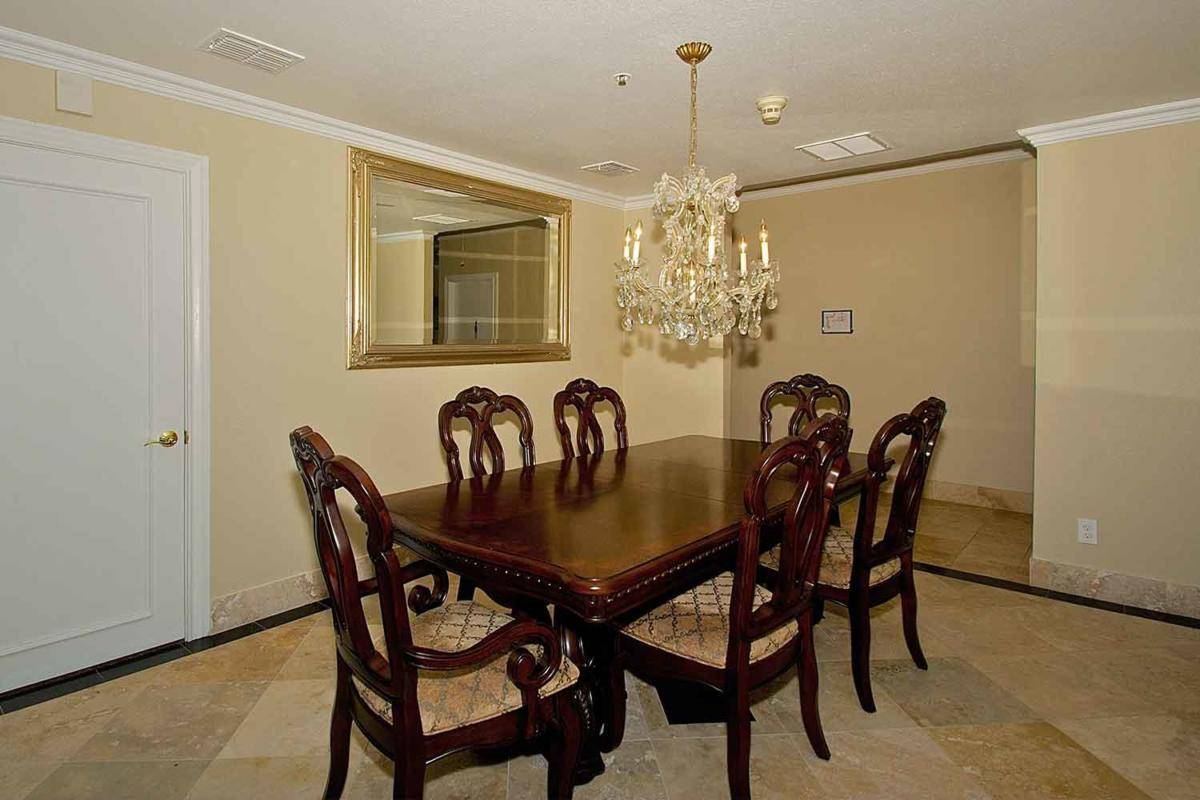 A dining room featuring a classic wooden table, six intricately carved chairs, a large mirror, and an elegant chandelier.