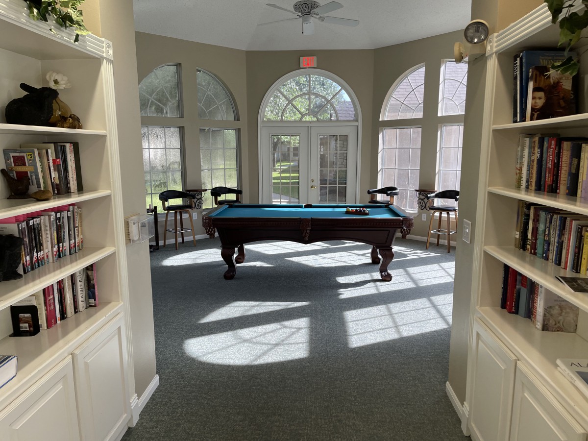 A sunlit game room featuring a pool table surrounded by large windows.