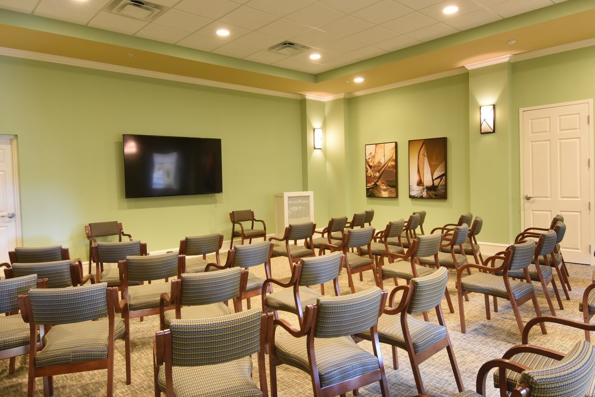 An empty conference room with rows of chairs facing a large television on the wall.