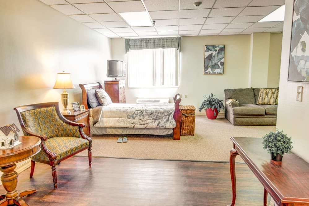 A spacious bedroom with a cozy bed, stylish chairs, and a comfortable sofa, enhanced by warm lighting and decorative plants.
