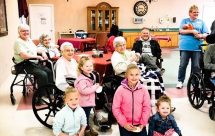 A group of children and seniors gather together indoors, sharing smiles and warmth.