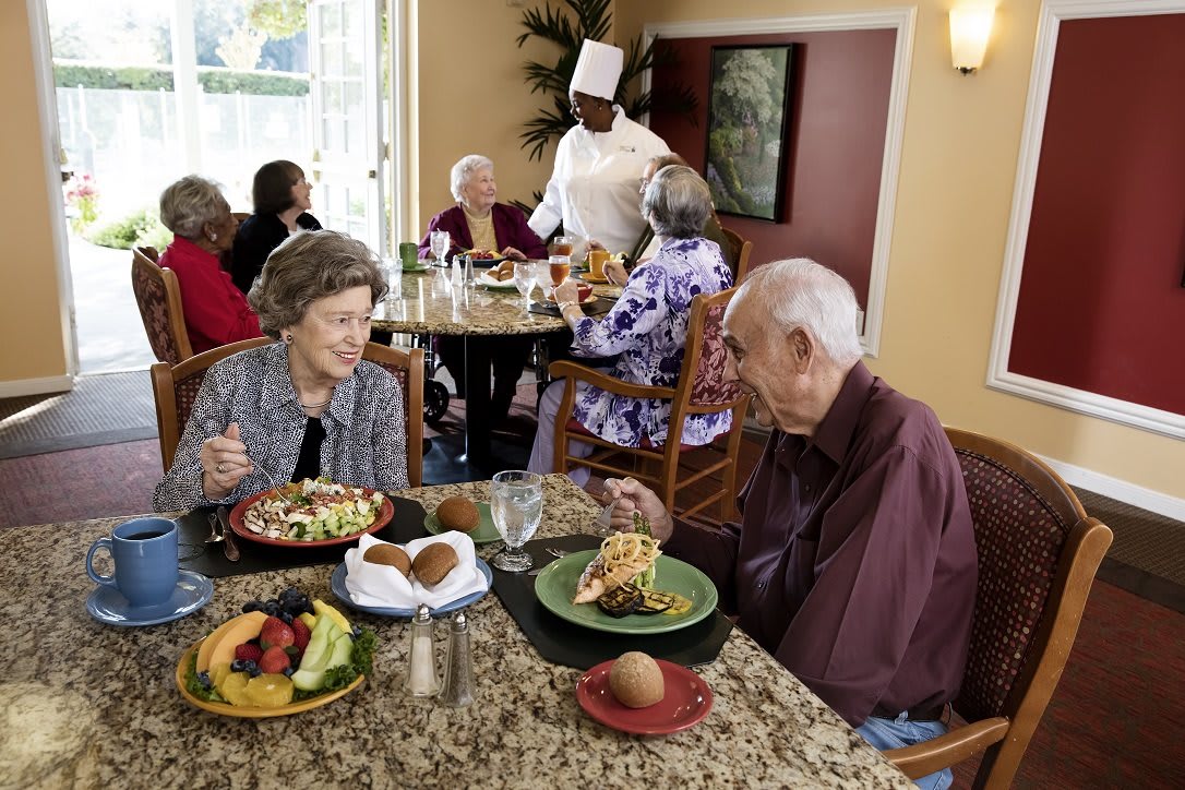 Elderly individuals enjoying a meal together at a restaurant, served by a chef.