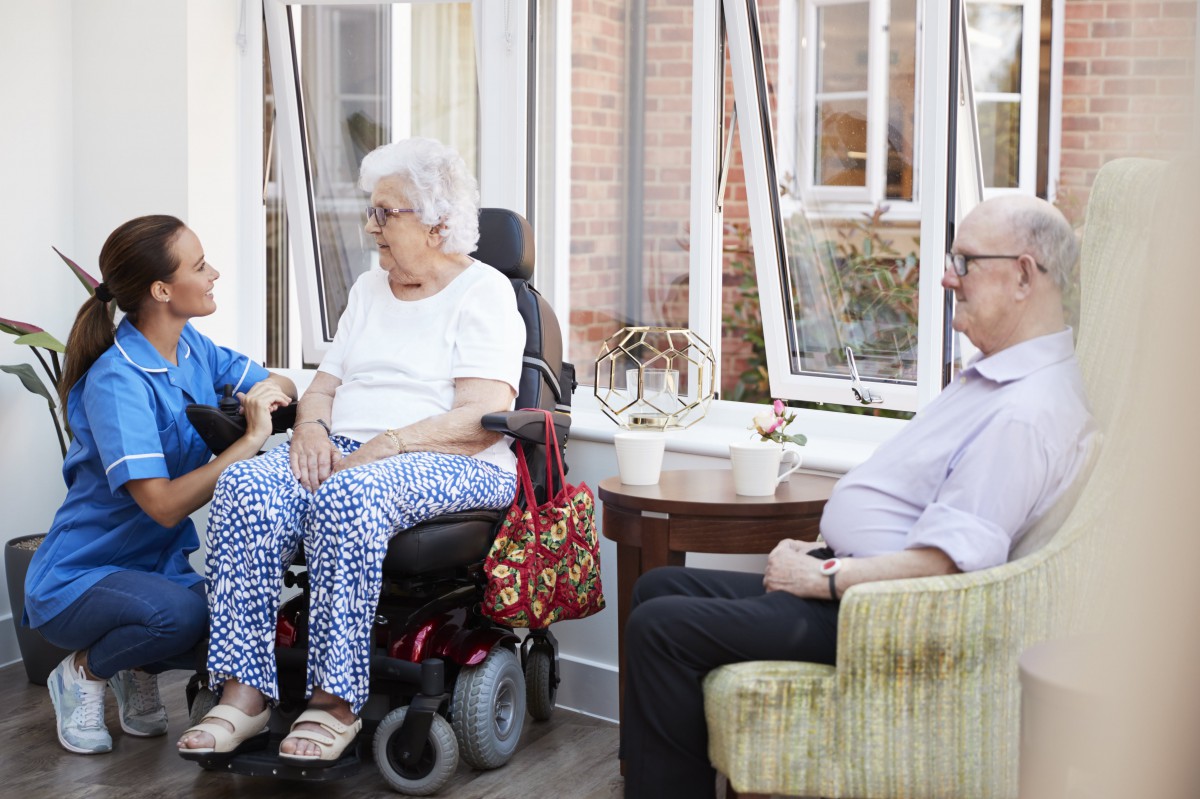 A casual conversation among seniors at a care home, with one person using a wheelchair.