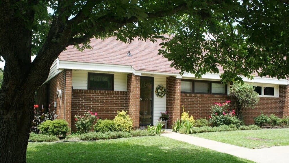 A charming brick house with a well-maintained garden and lush trees.
