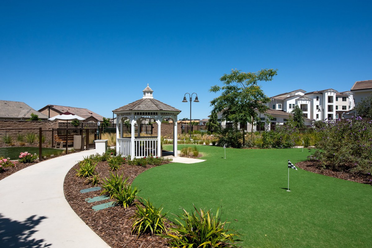 A well-maintained garden with a gazebo and landscaped pathways under a clear blue sky.