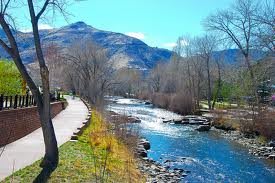 A scenic view of a river flowing alongside a mountain, with bare trees lining a pathway.