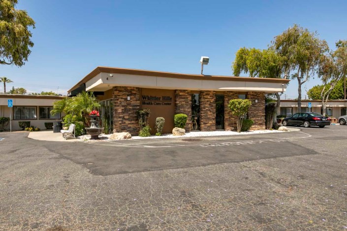 A small restaurant building with stone accents surrounded by plants on a sunny day.