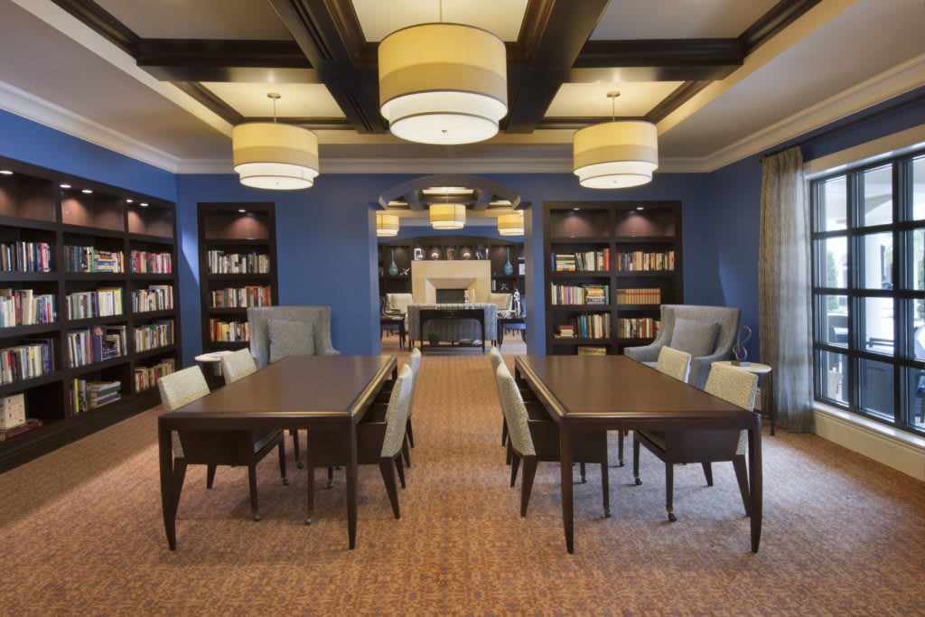 A well-lit library with tables and chairs, surrounded by bookshelves.