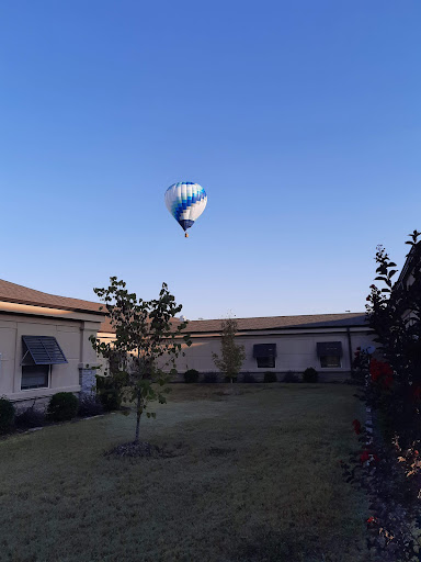 A hot air balloon floats gently in the blue sky above a serene courtyard.