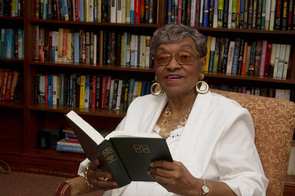 An elderly woman reading a book in a library.