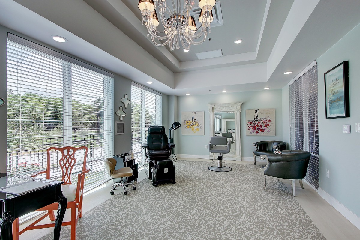 A modern salon interior with stylish chairs, a chandelier, and large windows letting in natural light.