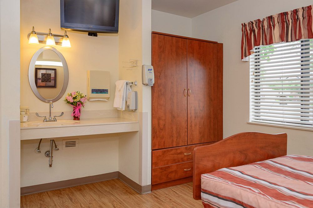 A cozy bedroom with a wooden wardrobe, a bed, and a vanity area featuring a sink and mirror.