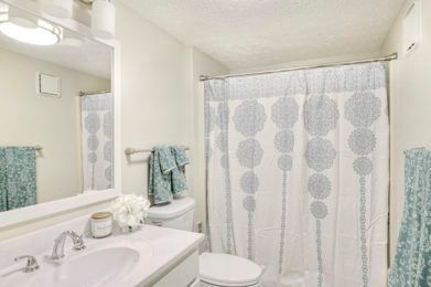 A clean and bright bathroom with a patterned shower curtain and neatly arranged towels.