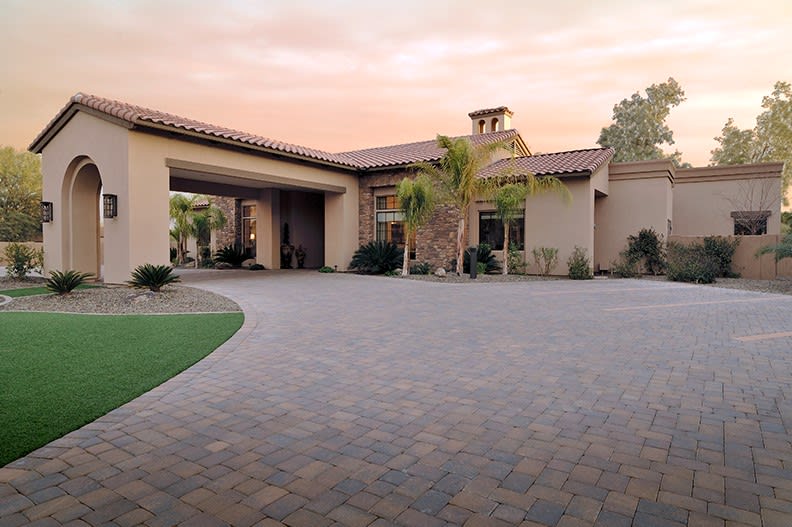 A beautiful house with a spacious driveway and palm trees at sunset.