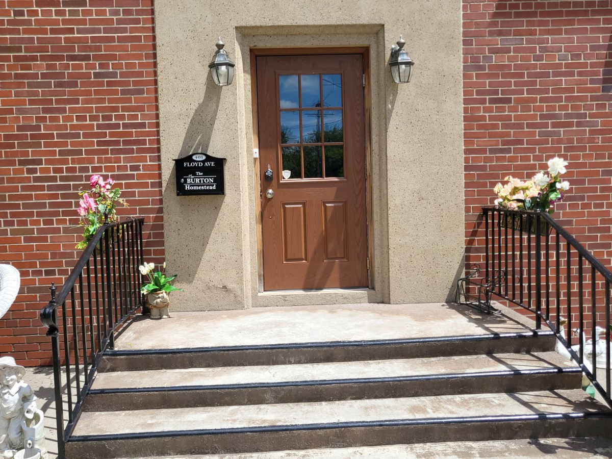 A brick building entry with steps leading to a wooden front door, adorned with flowers and outdoor lights.