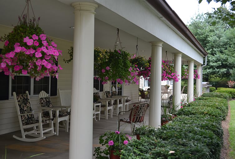 A charming porch with columns, adorned with hanging pink flowers and outdoor seating.