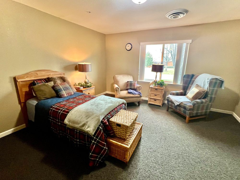 A cozy bedroom with a neatly made bed, armchairs, and warm lighting.