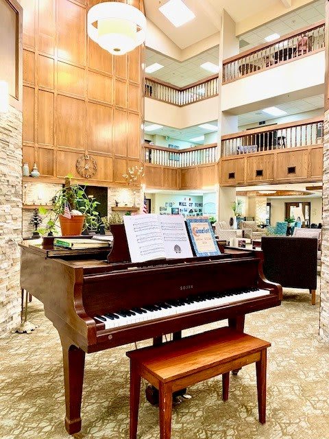 A grand piano with sheet music in a spacious lobby featuring wood paneling and elegant decor.