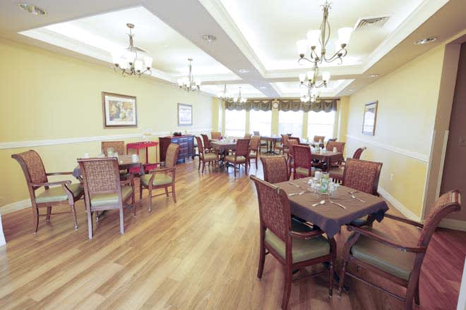 A well-lit dining room with multiple tables and chairs, featuring chandeliers and hardwood flooring.