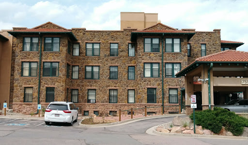 A view of a stone apartment building featuring multiple windows and a parking area in front.