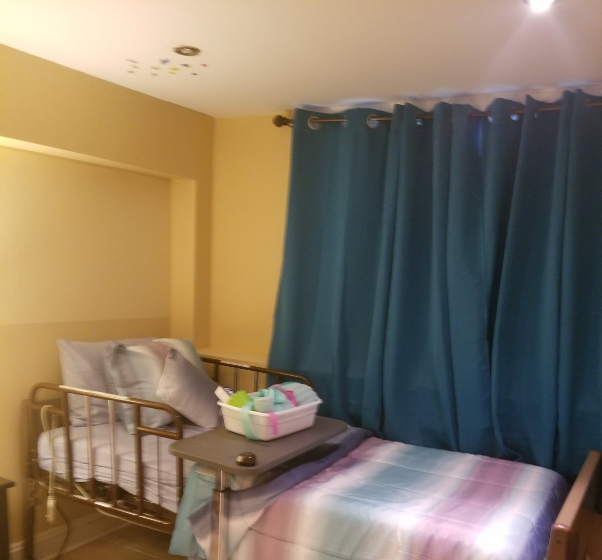 A cozy bedroom with a baby crib, teal curtains, and colorful blanket.
