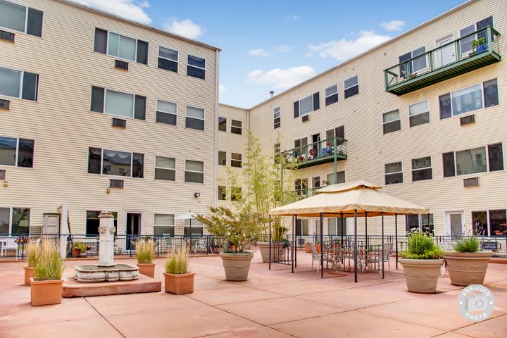 A courtyard of an apartment building featuring outdoor seating and potted plants.