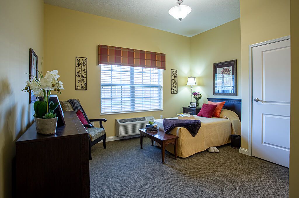 A cozy bedroom interior with a neatly made bed, bedside lamp, and large window.