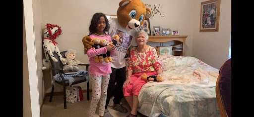 A joyful moment shared between a child, a person in a bear costume, and an elderly woman, surrounded by stuffed animals.
