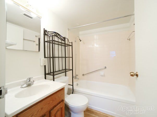 A small bathroom featuring a bathtub with a curtain, toilet, sink with a mirror above, and a black metal shelving unit.