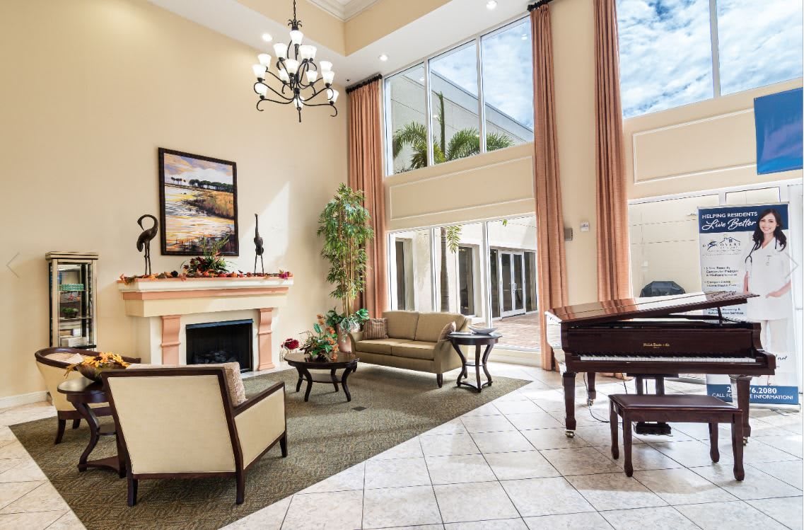 A spacious and well-lit lobby area featuring comfortable seating, a fireplace, large windows, and elegant decor.