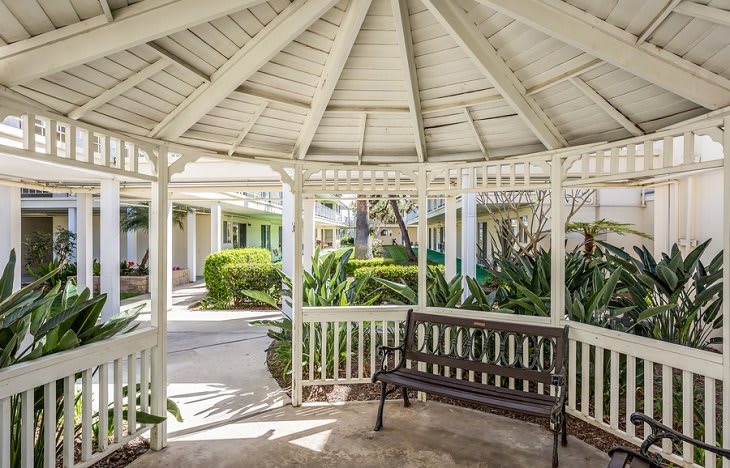 A peaceful gazebo with a bench surrounded by lush garden greenery.