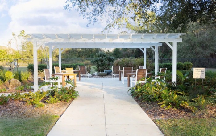 A tranquil outdoor garden area featuring a pergola with seating and lush landscaping.