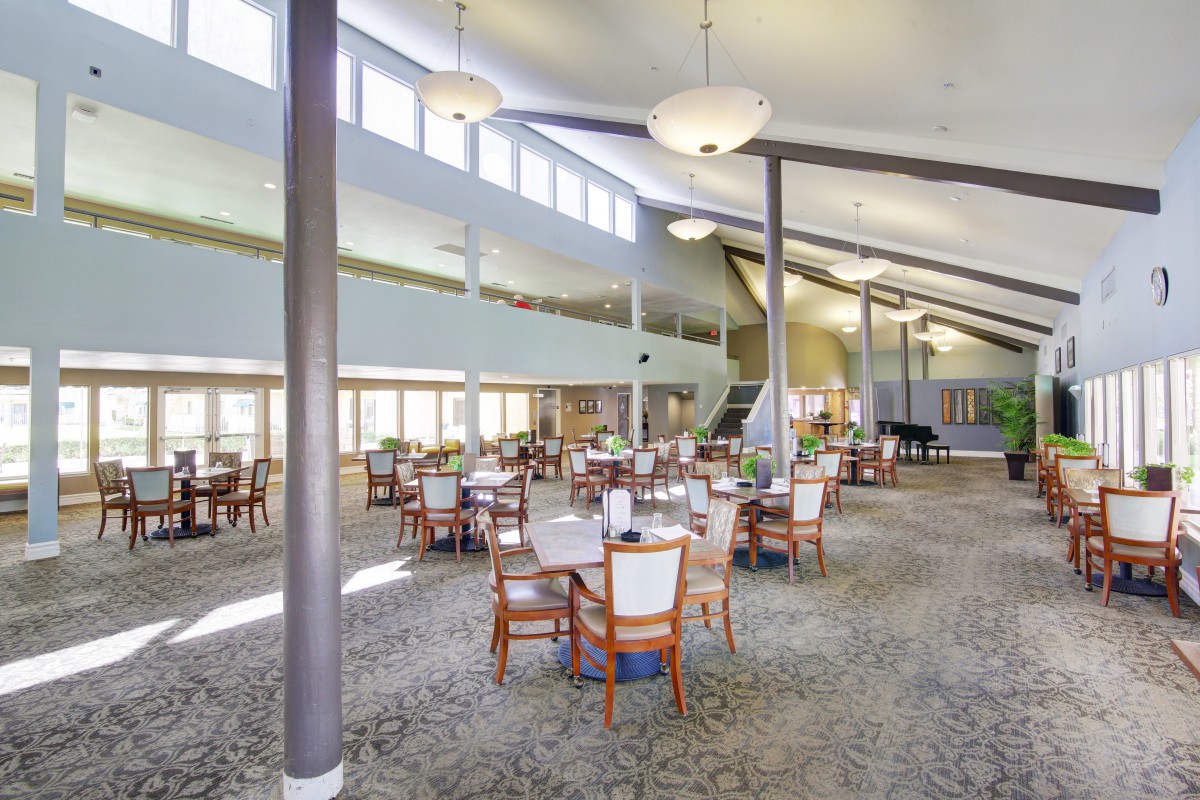 Spacious dining hall with tables and chairs, featuring high ceilings and large windows.