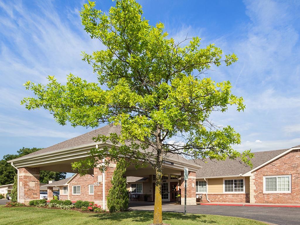 A brick building surrounded by greenery with a tree in the foreground under a clear blue sky.