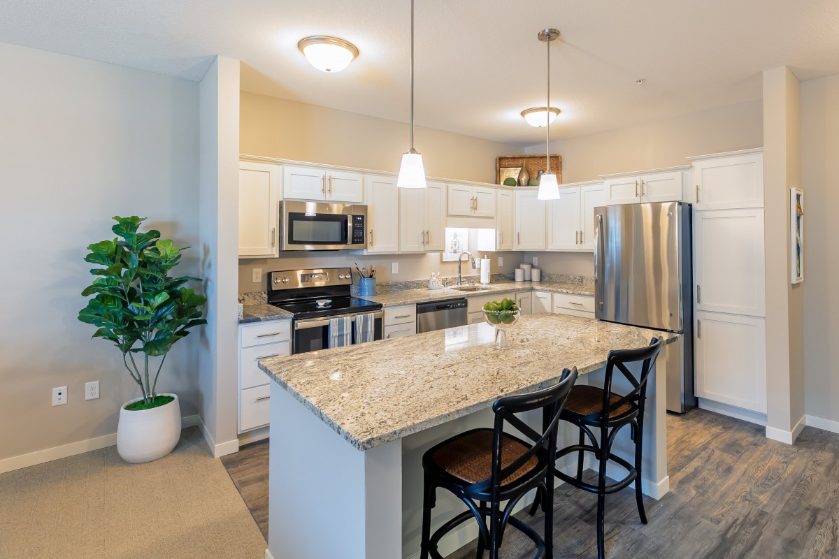 A modern kitchen featuring granite countertops, stainless steel appliances, and pendant lighting over an island with bar stools.