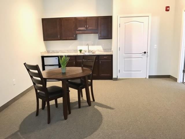 A minimalist dining area with a small table and chairs in front of a kitchenette.