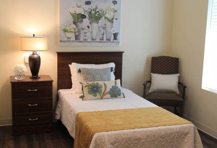 A cozy bedroom with a single bed, decorative pillows, and a floral painting on the wall.