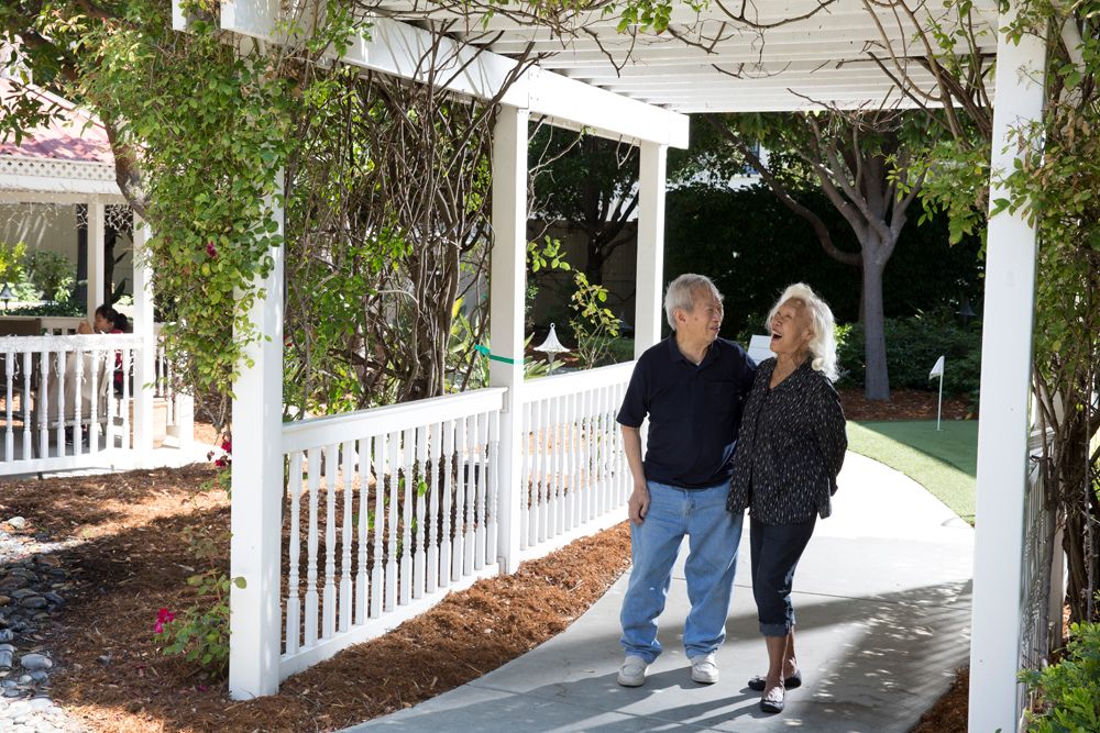 A couple walks together outside under a gazebo in a garden.